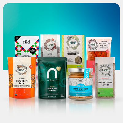 8 products on blue background: bombay protein mix, spirulina powder, nut butter, whole green lentils, mixed beans, noodles, seeds and a ready meal